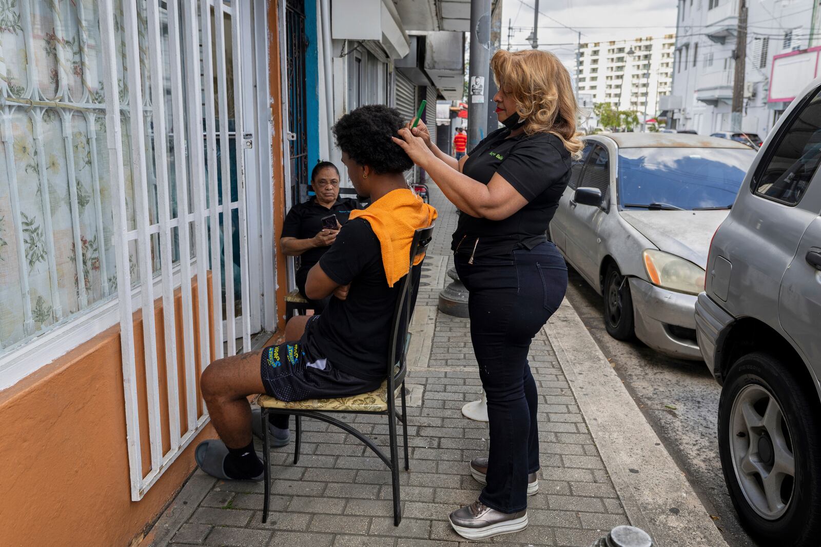 Nurys Perez, owner of Nurys Salon, styles a client's hair on the sidewalk outside her shop during a blackout in San Juan, Puerto Rico, Thursday, April 17, 2025. (AP Photo/Alejandro Granadillo)