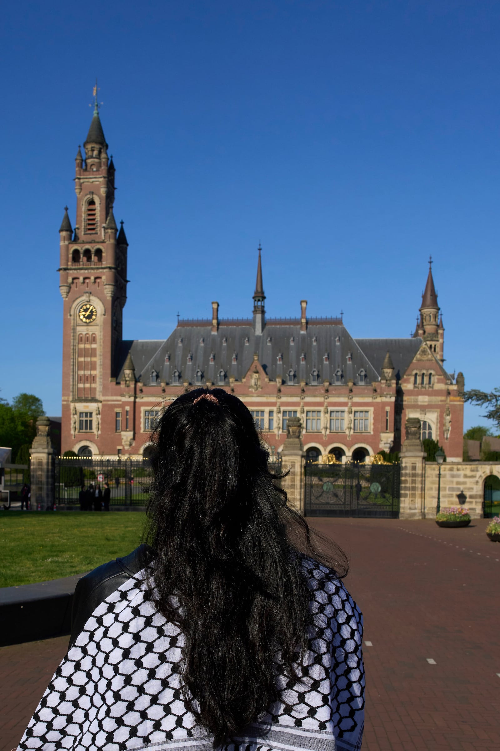 A woman wearing a keffieh stands in front of the International Court of Justice which opens hearings into a United Nations request for an advisory opinion on Israel's obligations to allow humanitarian assistance in Gaza and the West Bank, in The Hague, Netherlands, Monday, April 28, 2025. (AP Photo/Peter Dejong)
