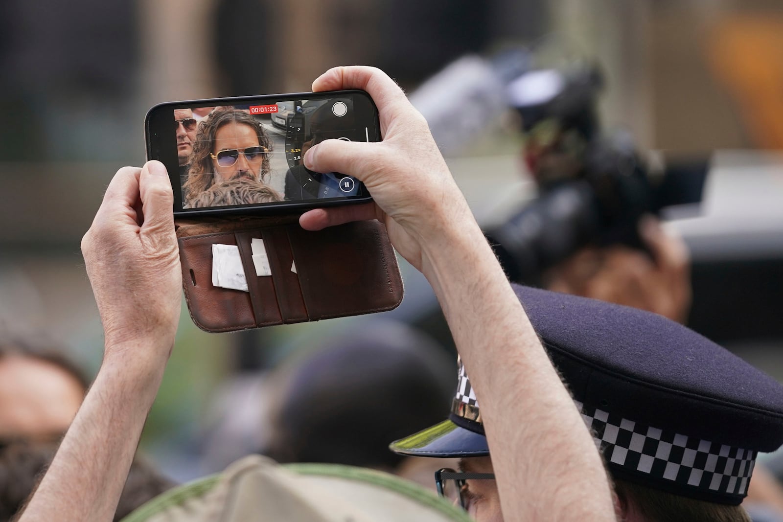 A person takes a smart phone picture as Russell Brand arrives at Westminster Magistrates' court in London, Friday, May 2, 2025, where he faces, rape and sexual assault charges involving four women. (AP Photo/Alberto Pezzali)