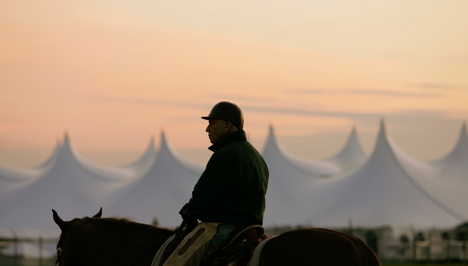 FILE - Trainer D. Wayne Lukas sits atop his horse as he watches morning workouts against the backdrop of a large tent set up in the infield before sunrise at Churchill Downs in Louisville, Ky., April 25, 2009. (AP Photo/Ed Reinke, file)