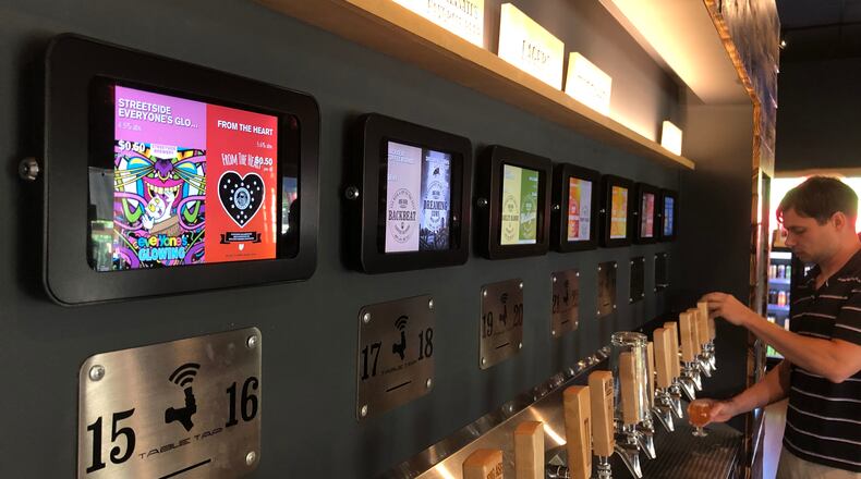 Pour House in Hamilton, which expects to open in January at The Marcum, will have a similar serving style to Big Ash Brewery in Cincinnati, where customers pour their own drinks and can see on the screens above them how many ounces they have dispensed, and the cost so far. MIKE RUTLEDGE/STAFF