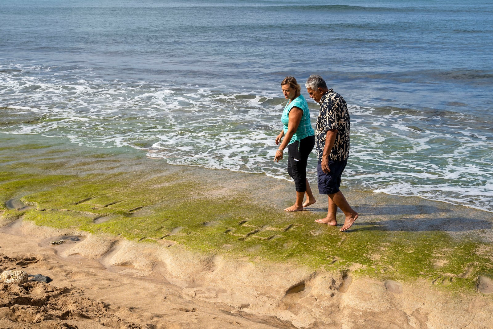 Archaeologist Laura Gilda of the U.S. Army Garrison Hawaii Environmental Division, left, and cultural practitioner Glen Kila walk along the shoreline near exposed petroglyphs at Pokai Bay, July 22, 2025, in Waianae, Hawaii. (AP Photo/Mengshin Lin)