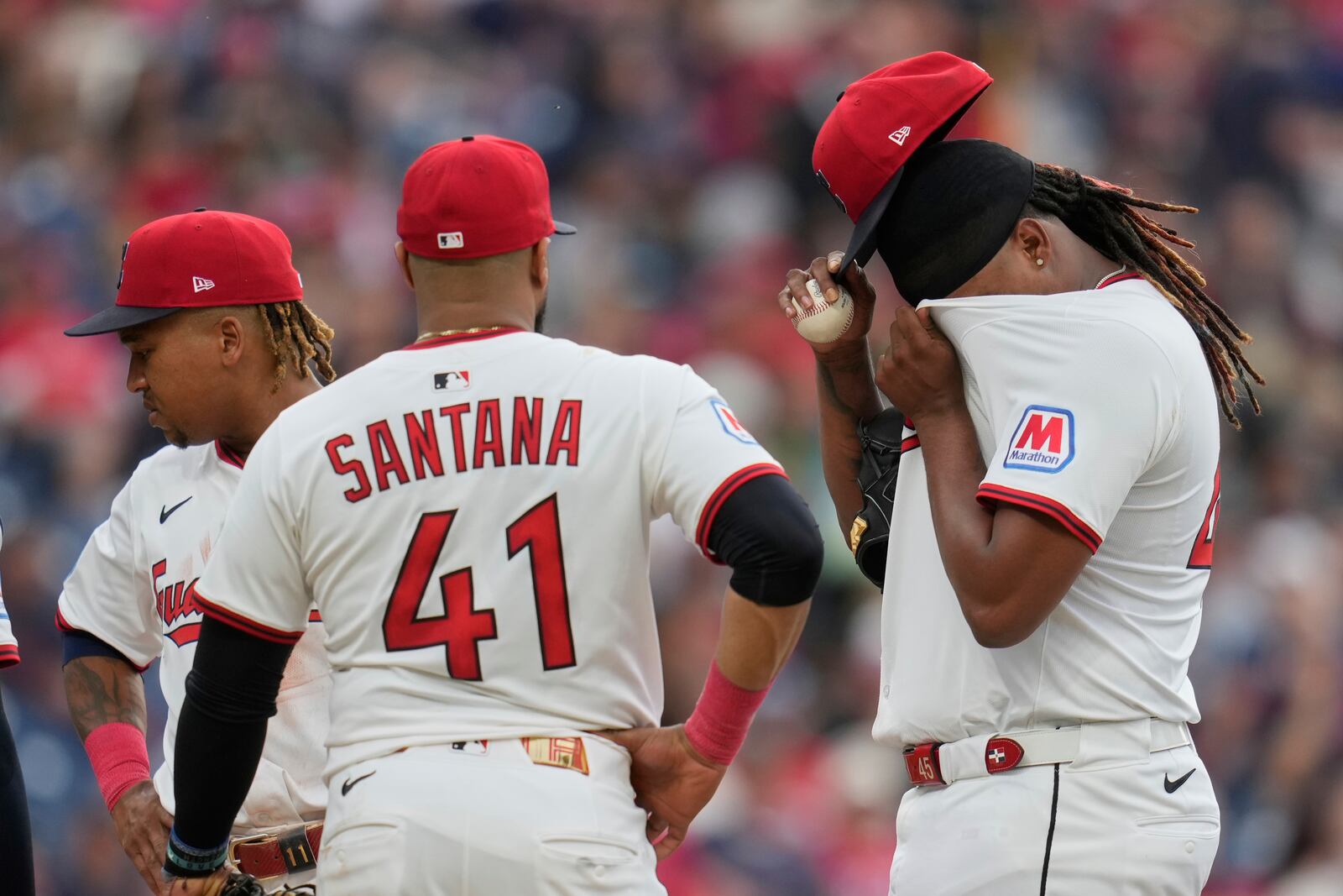 Cleveland Guardians starting pitcher Luis Ortiz, right, wipes his face with his jersey as he waits with teammates Jose Ramirez, left, and Carlos Santana (41) for Carl Willis during a mound meeting in the fifth inning of a baseball game against the Cincinnati Reds in Cleveland, Monday, June 9, 2025. (AP Photo/Sue Ogrocki)