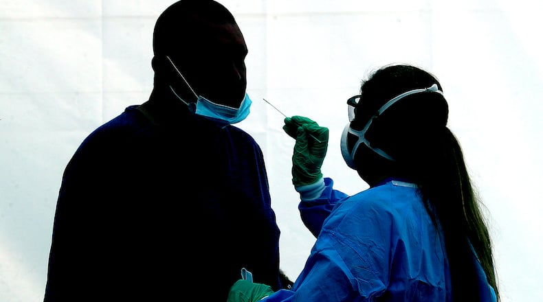 A man is silhouetted against the wall of a white tent, illuminated by the sun, as he gets a COVID-19 test at the Clark County Combined Health District's free COVID testing clinic at Hayward Middle School.