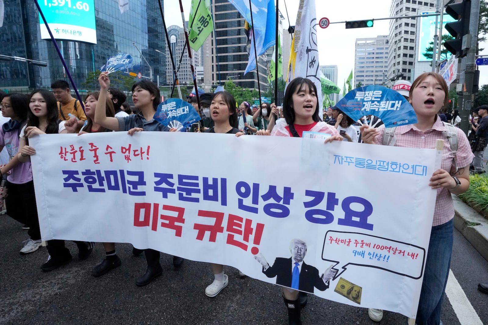 Supporters of the South Korean Confederation of Trade Unions march during a rally against the government's labor policy and U.S. President Donald Trump's tariffs policy on South Korea, in Seoul, South Korea, Saturday, July 19, 2025. The banner reads "We Condemn U.S. for forcing the the costs of station U.S. troops in South Korea!."(AP Photo/Ahn Young-joon)