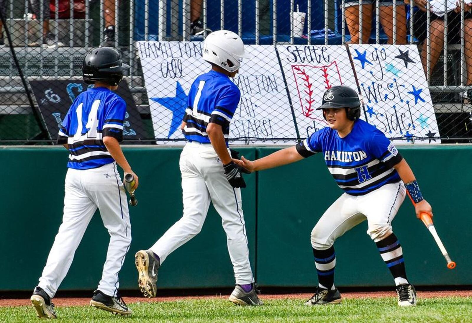 Hamilton West Side’s Blake Detherage (right) greets teammates Braedyn Moore (1) and Nick Brosius (14) during Monday’s 10-2 win over Grosse Pointe Woods-Shores (Mich.) in the Little League Great Lakes Regional at Grand Park Sports Campus in Westfield, Ind. NICK GRAHAM/STAFF