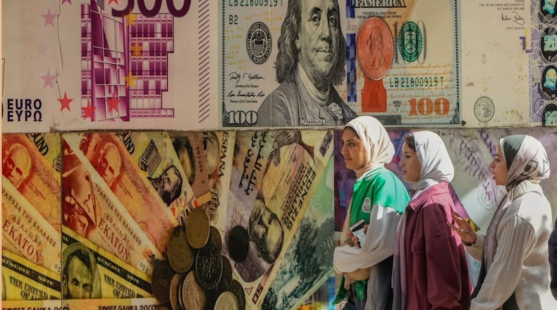 FILE - Egyptians walk past a poster depicting U.S. dollars and other currencies outside an exchange office in Cairo, Egypt, Thursday, Jan. 12, 2023. (AP Photo/Amr Nabil, File)