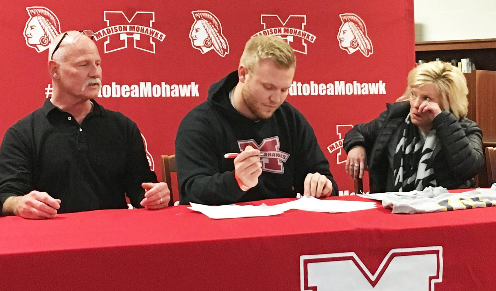 Madison’s Max Evans signs with the East Tennessee State University football program Friday afternoon in the high school media center as his parents, Greg and Julie, watch. RICK CASSANO/STAFF