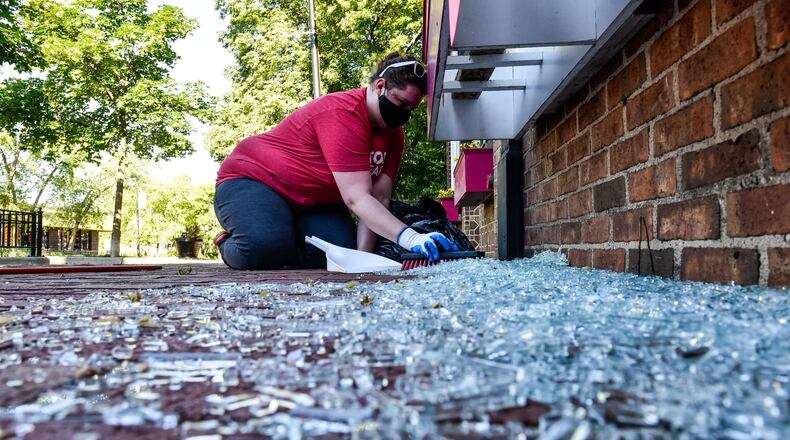 Jordan Buffington, from Beavercreek, cleans up glass from a broken window at Lily’s Bistro Sunday morning in the Oregon District. Signs, debris and graffiti damage were left in downtown Dayton Sunday morning, May 31, after protests throughout the day on Saturday in the aftermath of the death of George Floyd. CIty and county workers, business owners and volunteers spent the morning sweeping up glass and scrubbing spray paint. NICK GRAHAM / STAFF