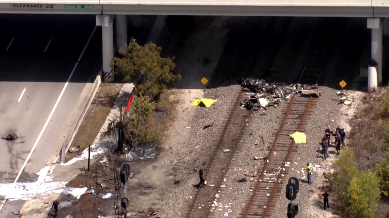 In this image taken from video provided by WSVN-TV, emergency personnel respond to the area where a small plane crashed on the railroad tracks beneath the overpass near Interstate 95 in Boca Raton, Fla., Friday, April 11, 2025. (WSVN-TV via AP)