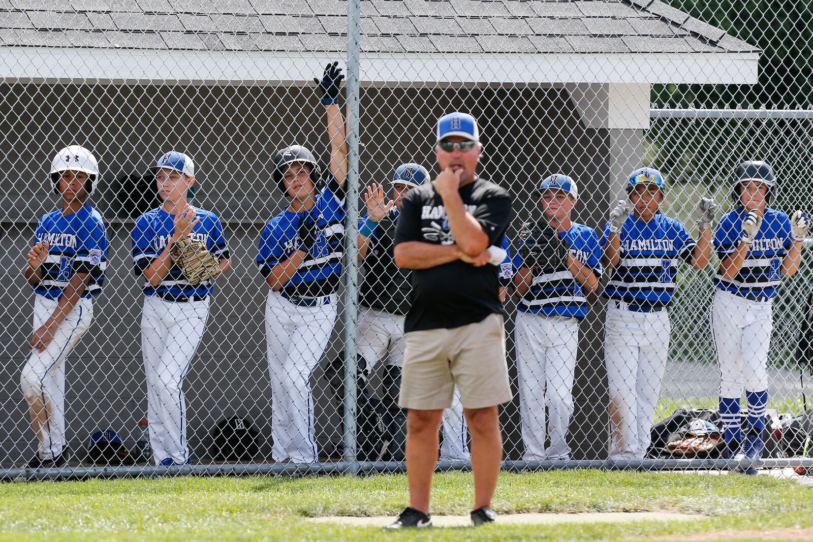 Hamilton West Side assistant coach Tim Nichting coaches third base as players watch from the dugout Thursday during the winners’ bracket final against Canfield in the Ohio Little League 12-year-old baseball tournament at Ford Park in Maumee. CONTRIBUTED PHOTO BY SCOTT GRAU