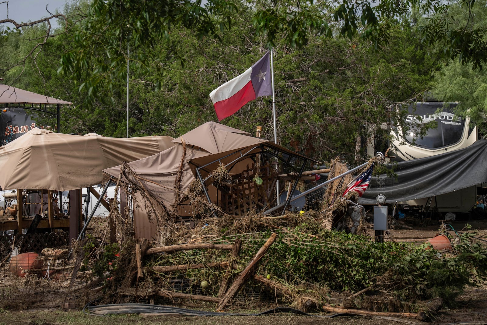 A Texas flag waves in the wind amongst debris from flash flooding at Cedar Stays RV Park in Marble Falls, Texas, Monday, July 7, 2025. (Mikala Compton /Austin American-Statesman via AP)