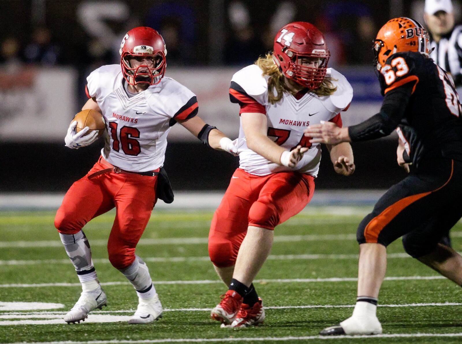 Madison’s Tyler Baumgartner carries the ball as Caleb Bolen blocks for him against Wheelersburg’s Nic Parsley (63) during Friday night’s Division V state semifinal at Herrnstein Field in Chillicothe. NICK GRAHAM/STAFF