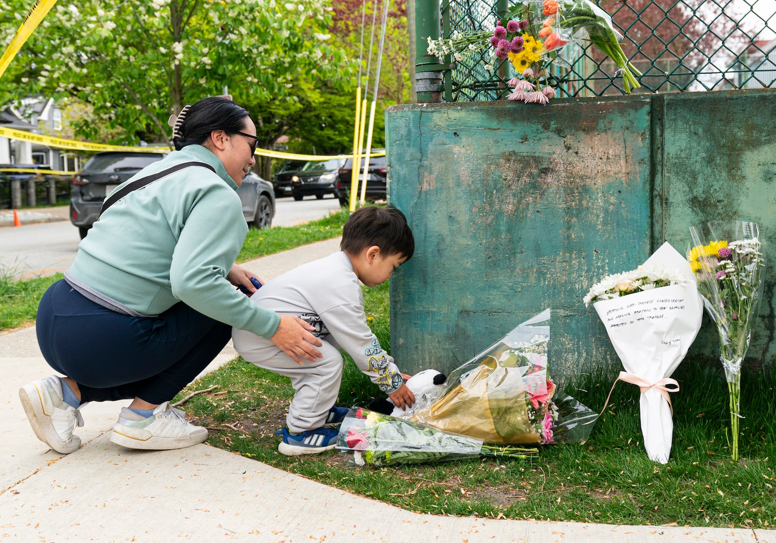 A young child and his mother leave a teddy bear and flowers, near the location where a vehicle drove into crowd at a street festival, in Vancouver, Sunday April 27, 2025. (Rich Lam/The Canadian Press via AP)