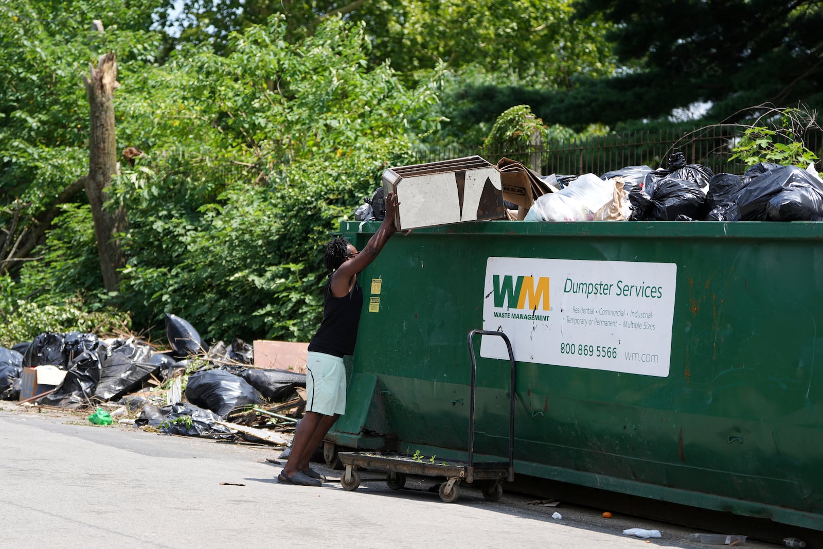 A man drops off trash at a garbage collection site, Wednesday, July 9, 2025, in Philadelphia. (AP Photo/Matt Slocum)