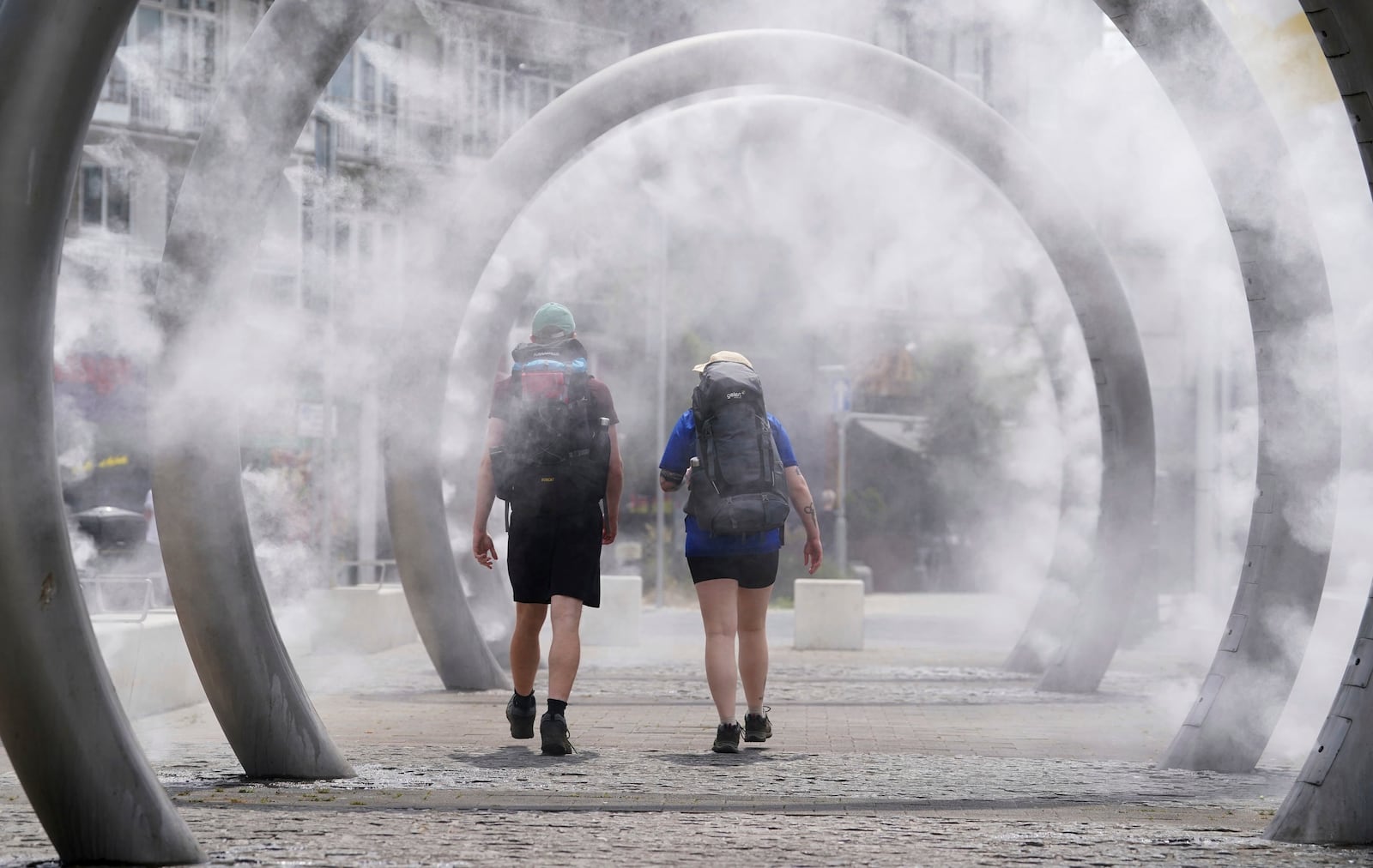 Walkers cool off as they walk through a water feature spraying a fine mist in Dover, England, Friday, June 20, 2025. (Gareth Fuller/PA via AP)