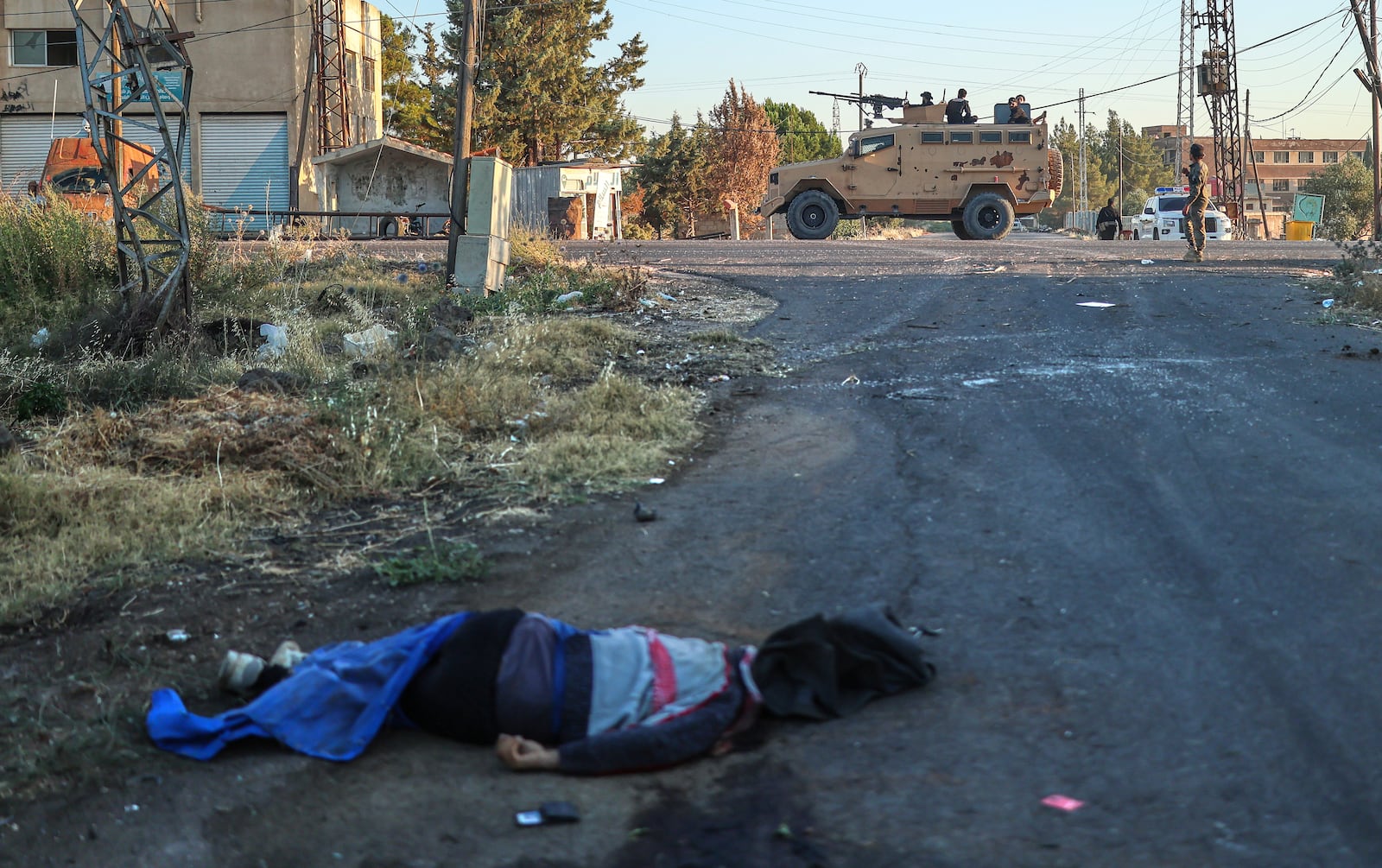 A dead fighter from the Druze militias lies on the ground, as Syrian government forces, background, deploy at Mazraa village on the outskirts of the city of Sweida, where clashes erupted between Sunni Bedouin clans and Druze militias, southern Syria, Monday, July 14, 2025. (AP Photo/Ghaith Alsayed)