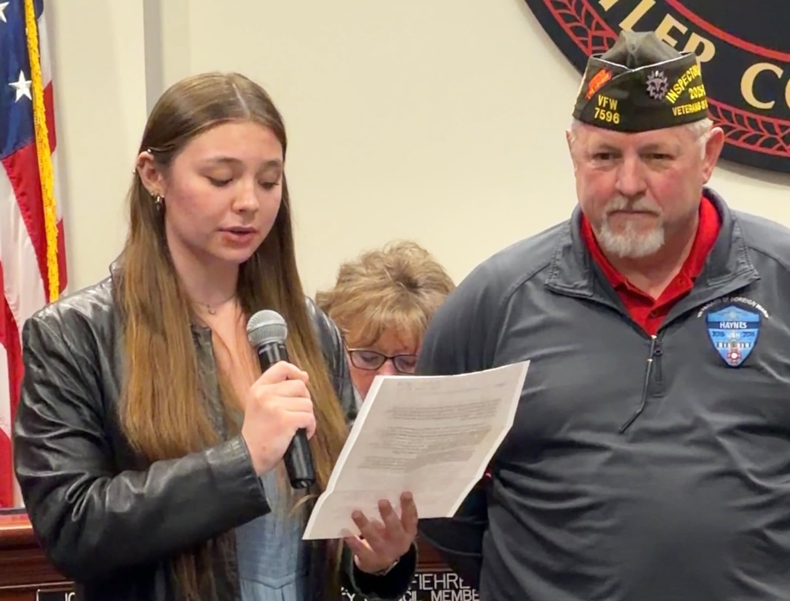Hamilton High School senior Kaitlyn Roberts (left) reads an essay that earned her a $20,000 Veterans of Foreign War scholarship as Chris Haynes, Hamilton’s assistant superintendent of street, fleet and sewers and a former VFW state commander, looks during a Hamilton City Council meeting Wednesday, Feb. 11, 2026. Roberts was honored by the city at the meeting. ERIC SCHWARTZBERG/STAFF
