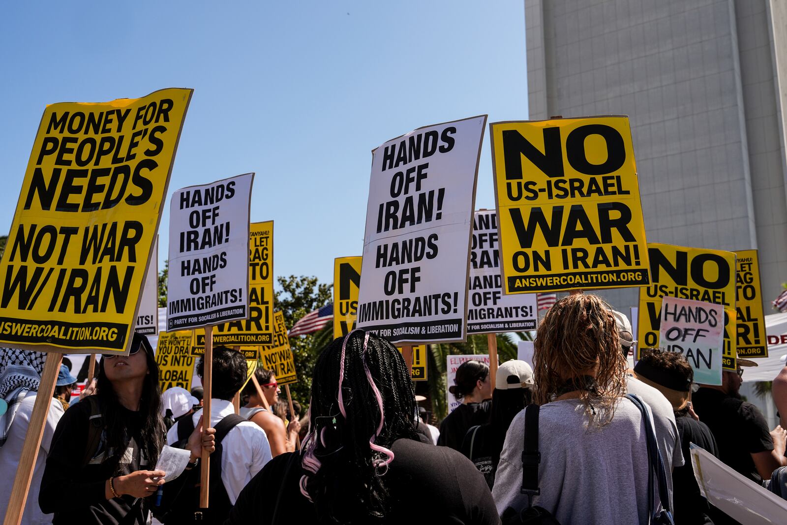 Two anti-war demonstrators hold signs outside the Wilshire Federal Building in Los Angeles Sunday, June 22, 2025, following U.S. airstrikes on Iran's nuclear facilities. (AP Photo/Jae C. Hong)