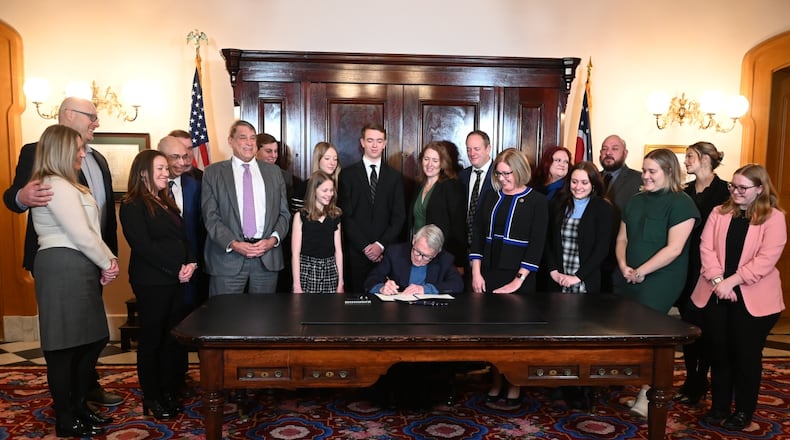 Lawmakers and advocates crowd around Ohio Gov. Mike DeWine on Wednesday, Jan. 8, 2025, as the Republican signs a bill establishing social "grooming" as a criminal offense in Ohio.
