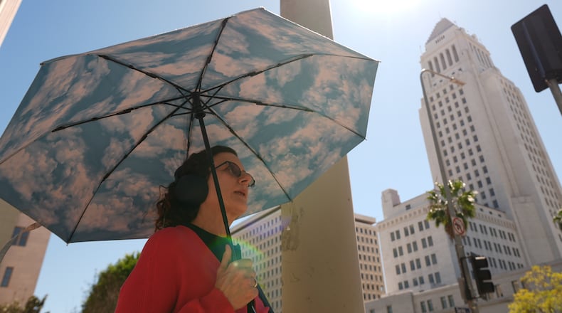 A pedestrian holds a cloud themed umbrella under a sunny day next to Los Angeles City Hall in Los Angeles Thursday, March. 12, 2026. (AP Photo/Damian Dovarganes)