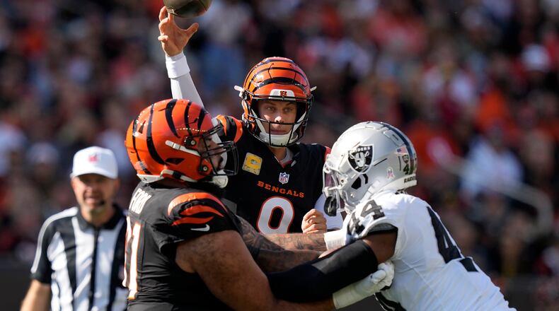 Cincinnati Bengals quarterback Joe Burrow, middle, passes as guard Cody Ford, left, blocks Las Vegas Raiders defensive end K'Lavon Chaisson during the first half of an NFL football game in Cincinnati, Sunday, Nov. 3, 2024. (AP Photo/Carolyn Kaster)