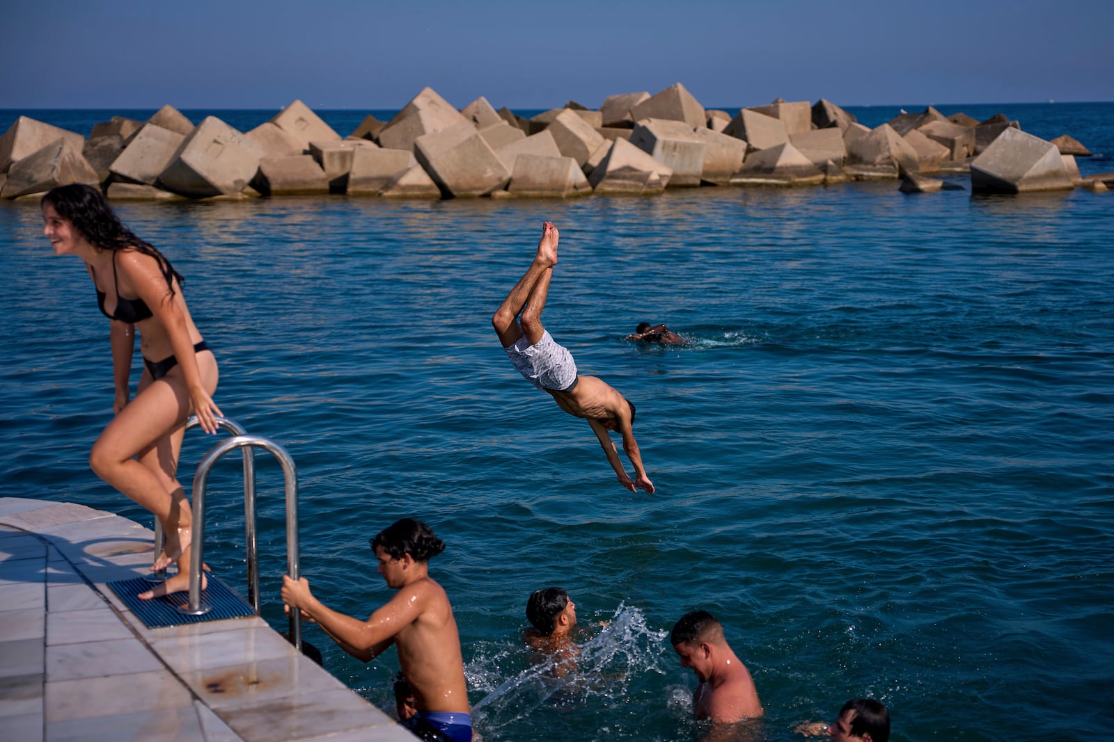 Swimmers jump into the water on a hot day in Barcelona, Spain, Tuesday, July 1, 2025. (AP Photo/Emilio Morenatti)