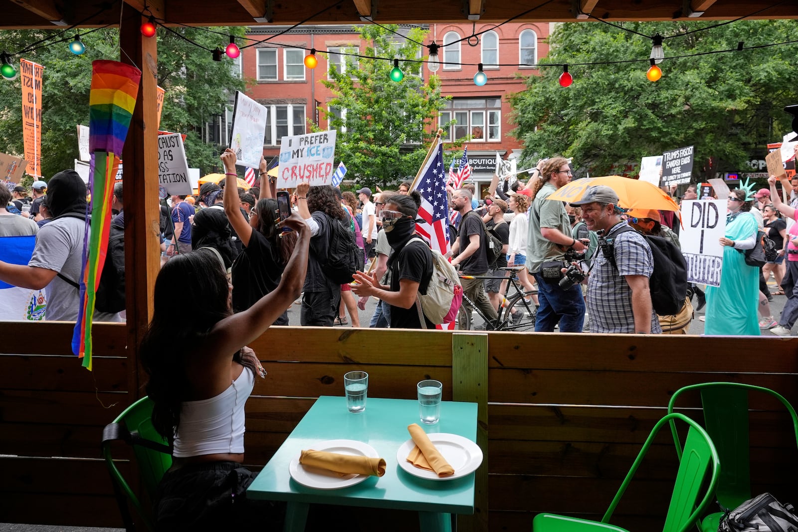 A person sitting in a restaurant records demonstrators as they march during a protest taking place on the day of a military parade commemorating the Army's 250th anniversary, coinciding with President Donald Trump's 79th birthday, Saturday, June 14, 2025, in Washington. (AP Photo/Alex Brandon)