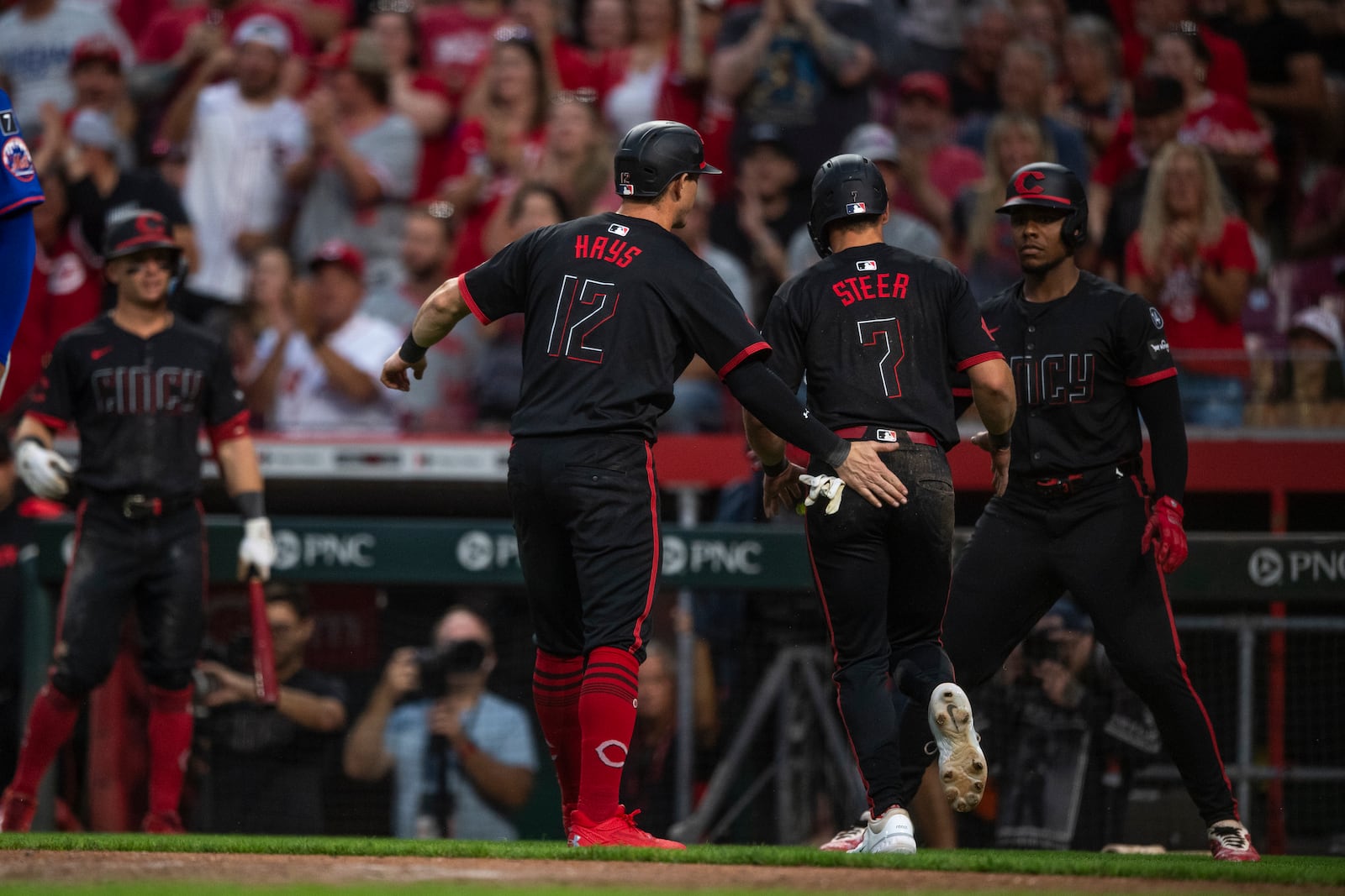 Cincinnati Reds' Austin Hays (12) congratulates Spencer Steer (7) after Steer slid into home in the fourth inning of a baseball game against the New York Mets, Friday, Sept. 5, 2025, in Cincinnati. (AP Photo/Michael Swensen)