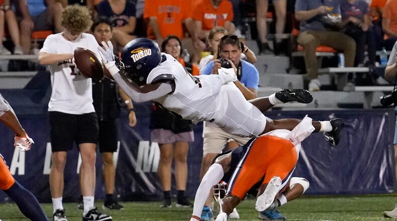 Toledo running back Peny Boone, dives over Illinois defensive back Xavier Scott, bottom center, for a touchdown during the second half of an NCAA college football game Saturday, Sept. 2, 2023, in Champaign, Ill. (AP Photo/Charles Rex Arbogast)