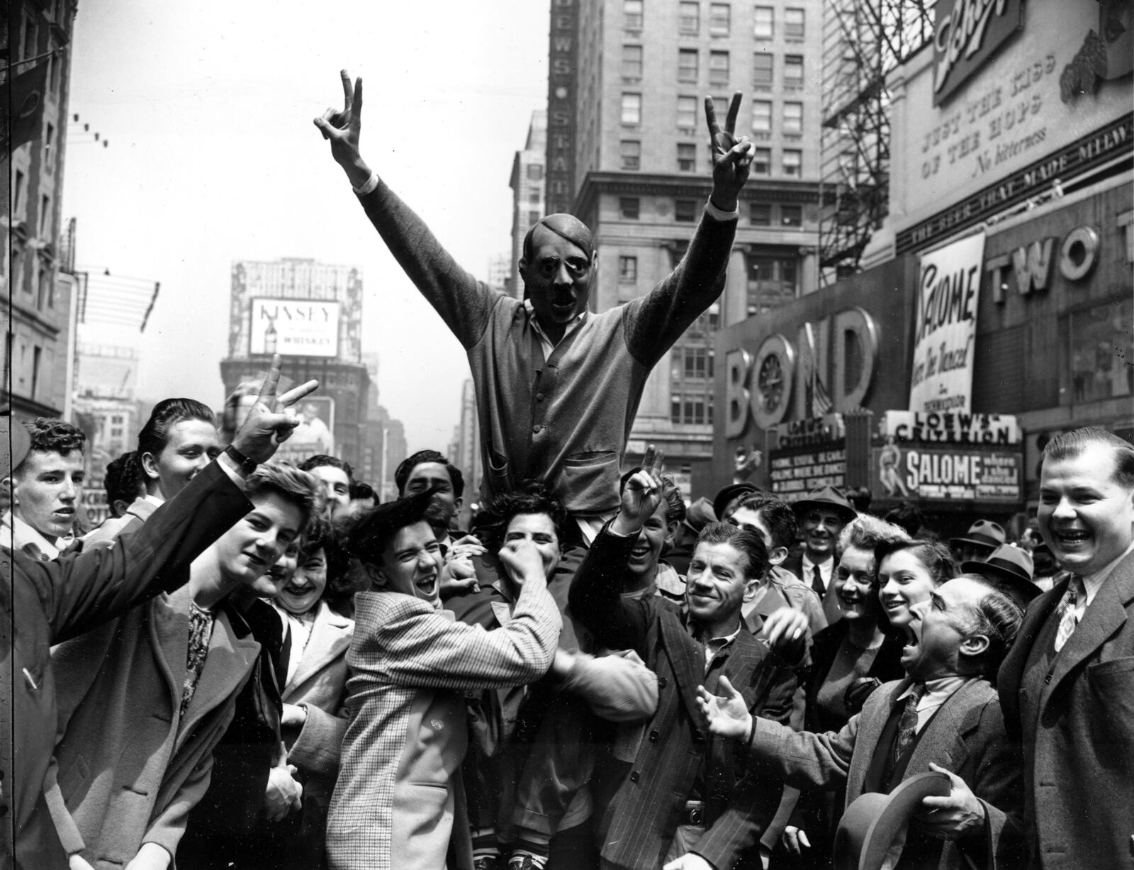 FILE - New Yorkers gather around a youth wearing a mask of Adolf Hitler to cheer the news of the surrender of Germany in New York's Times Square on May 7, 1945. (AP Photo/Harry Harris, File)
