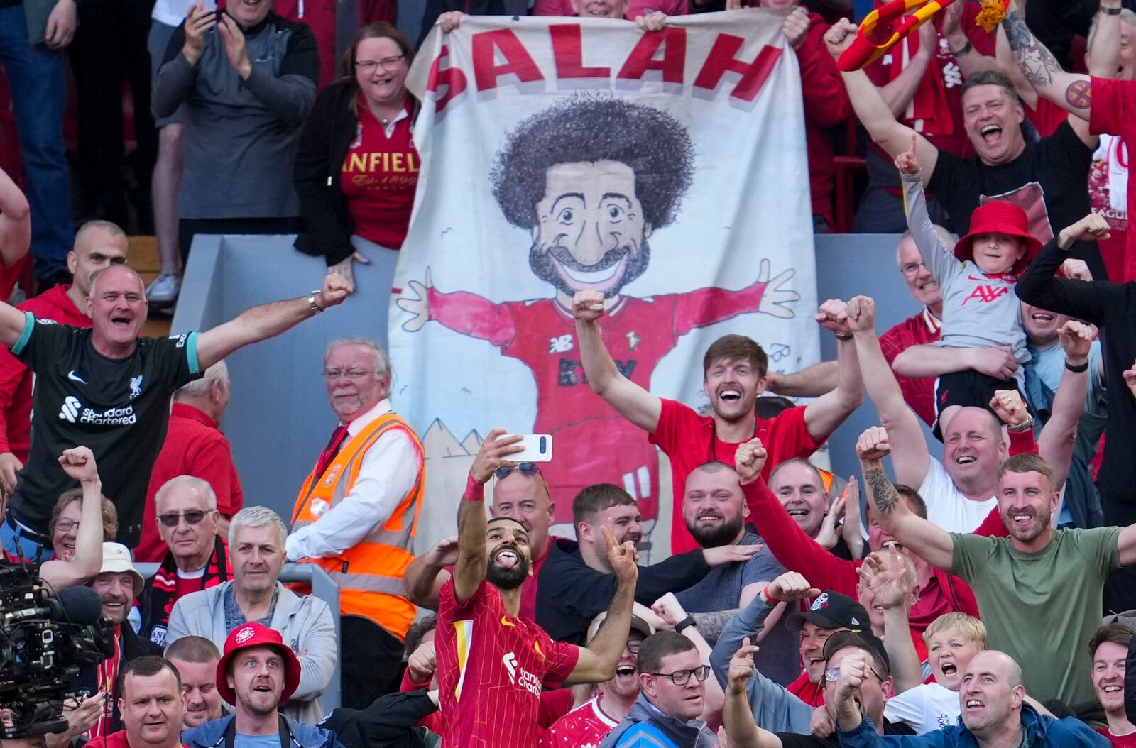 Liverpool's Mohamed Salah takes a selfie with a fans smartphone as he celebrates after scoring his side's fourth goal during the English Premier League soccer match between Liverpool and Tottenham Hotspur at Anfield in Liverpool, England, Sunday, April 27, 2025. (AP Photo/Jon Super)