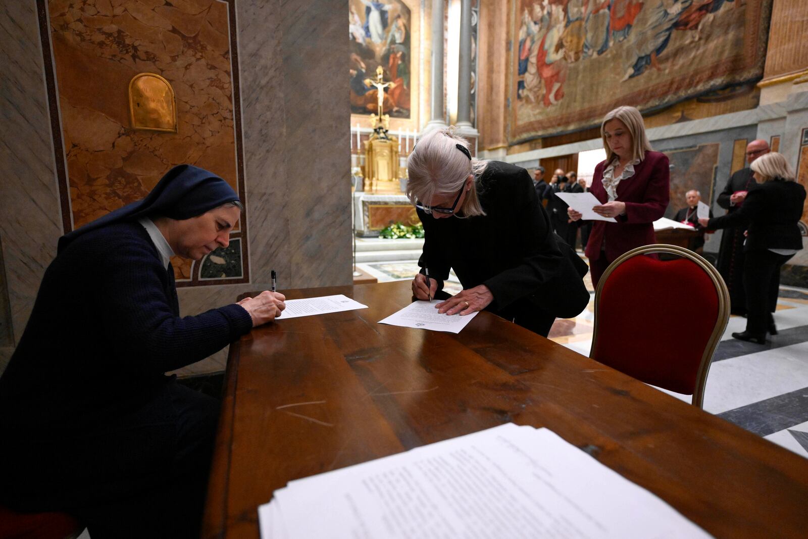In this image made available on Tuesday, May 6, 2025 by Vatican Media, Vatican employees sign the oath of secrecy for all those assigned to the conclave during a ceremony in the Pauline Chapel at the Vatican, Monday, May 5, 2025. (Vatican Media via AP)
