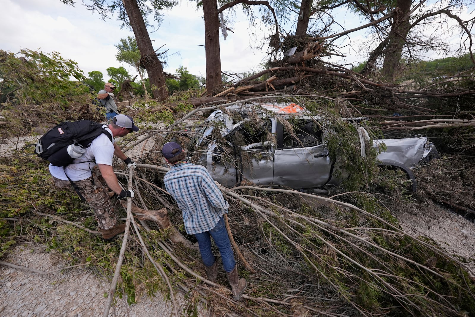 People search around a damaged truck and branches along the Guadalupe River after flooding in Kerrville, Texas on Wednesday , July 9, 2025. (AP Photo/Gerald Herbert)