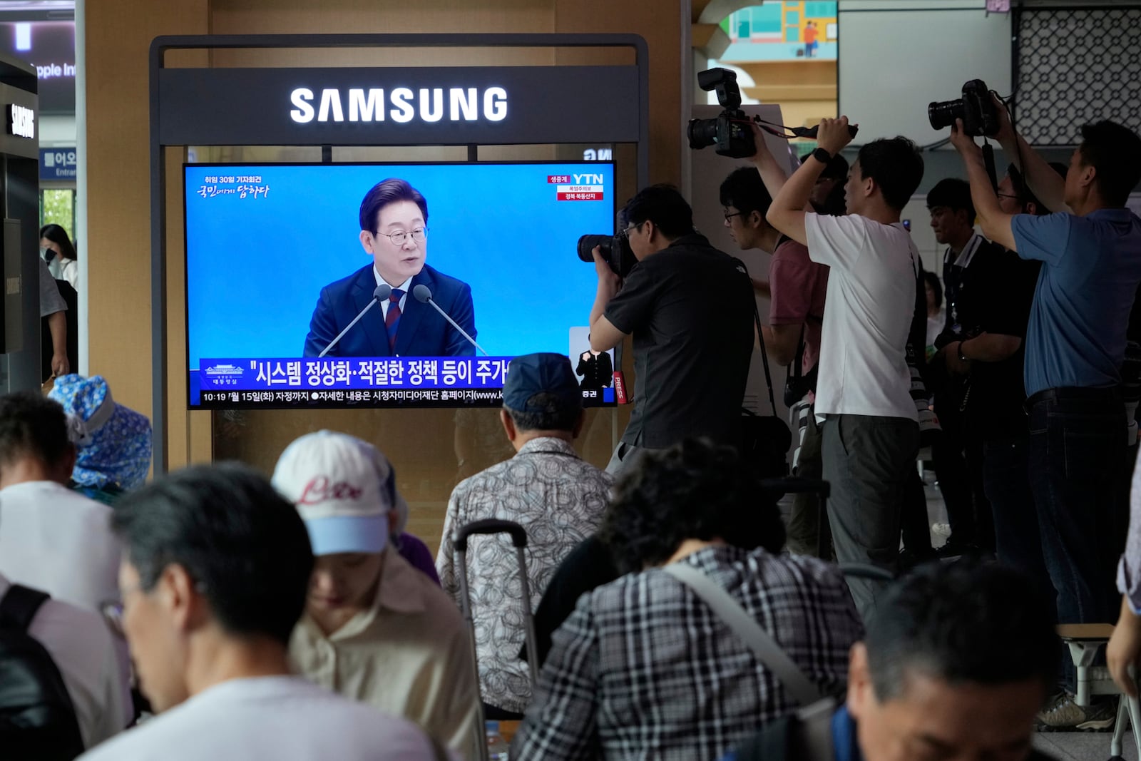 People watch a TV screen showing the live broadcast of South Korean President Lee Jae Myung's press conference at the Seoul Railway Station in Seoul, South Korea, Thursday, July 3, 2025. (AP Photo/Ahn Young-joon)