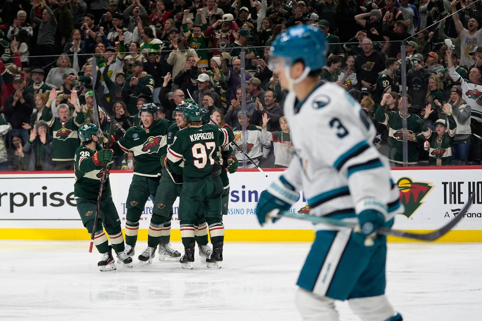 Minnesota Wild center Joel Eriksson Ek (14), middle, celebrates with teammates after scoring a goal as San Jose Sharks defenseman Henry Thrun (3), foreground, skates across the ice during the third period of an NHL hockey game, Wednesday, April 9, 2025, in St. Paul, Minn. (AP Photo/Abbie Parr)