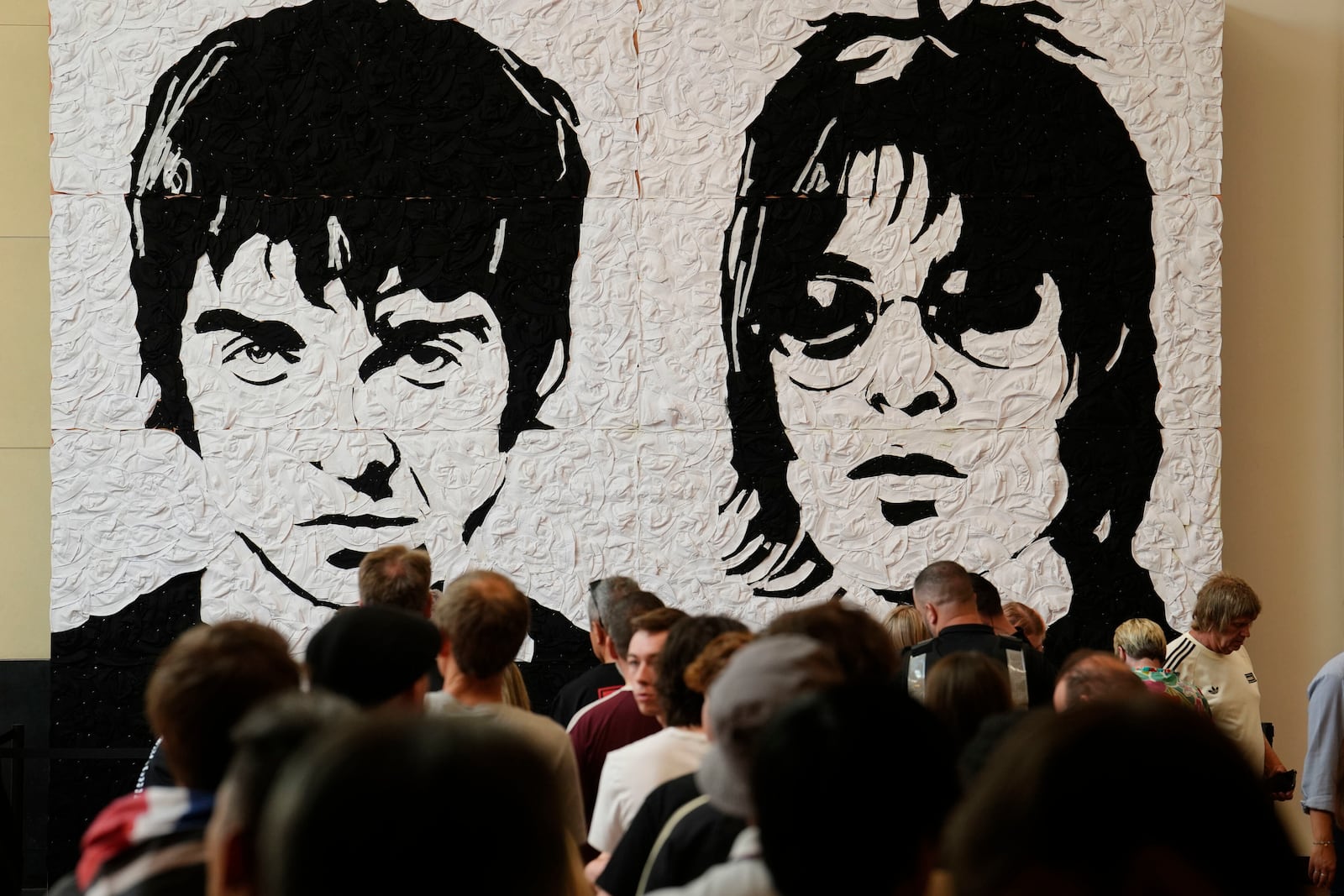 Oasis fans take photos in front of the Wonder Wall - a mural by Welsh artist Nathan Wyburn made out of 3,000 black and white bucket hats depicting Liam and Noel Gallagher - at the St David's shopping centre in Cardiff, ahead of the first show in their long-awaited reunion tour kicking off in Wales, Friday, July 4, 2025. (Jordan Pettitt/PA via AP)