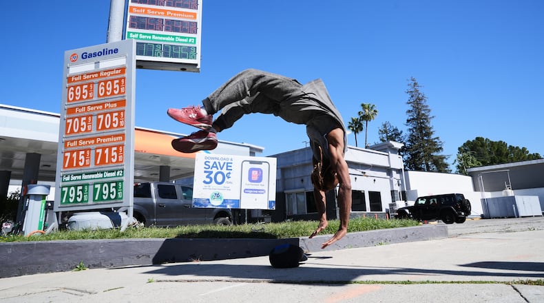 Marcus Hopkins, a street performer, does a backflip in front of advertised gas prices Monday, March 9, 2026, in Los Angeles. (AP Photo/Damian Dovarganes)