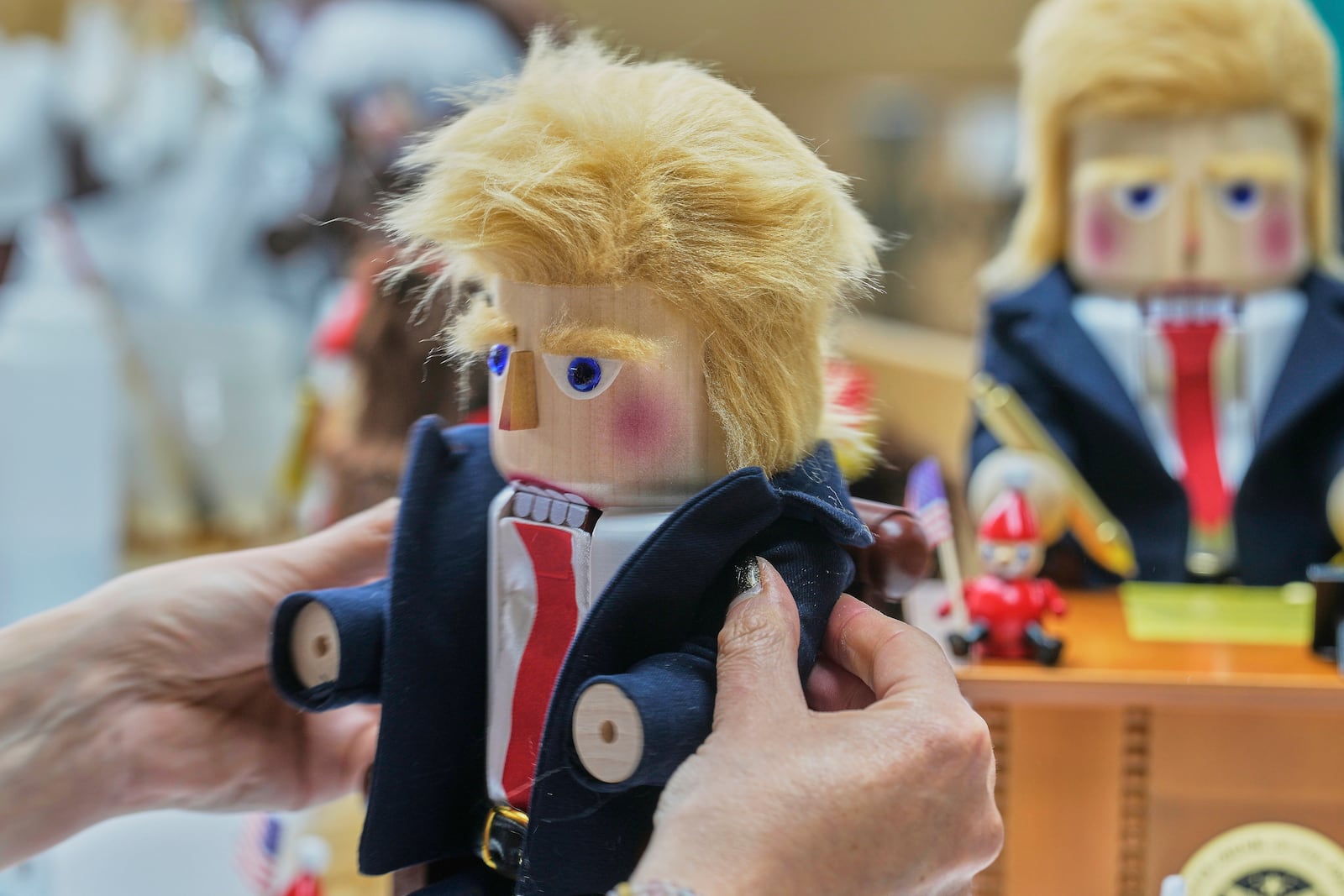 A woman fixes a coat on a nutcracker titled "Resolute Desk of the President," featuring a seated figure signing a "presidential proclamation," at the Steinbach-Volkskunst nutcracker factory in Marienberg, Germany, Tuesday, April 15, 2025. (AP Photo/Markus Schreiber)