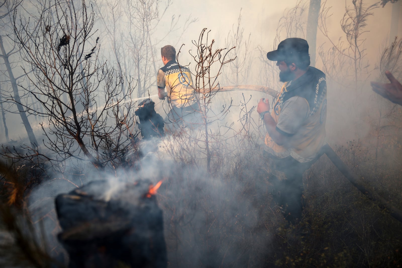 Emergency responders with the Syrian Civil Defense, known as the White Helmets, work to extinguish a wildfire near the town of Rabia, in Syria's Latakia countryside, Sunday, July 6, 2025. (AP Photo/Ghaith Alsayed)