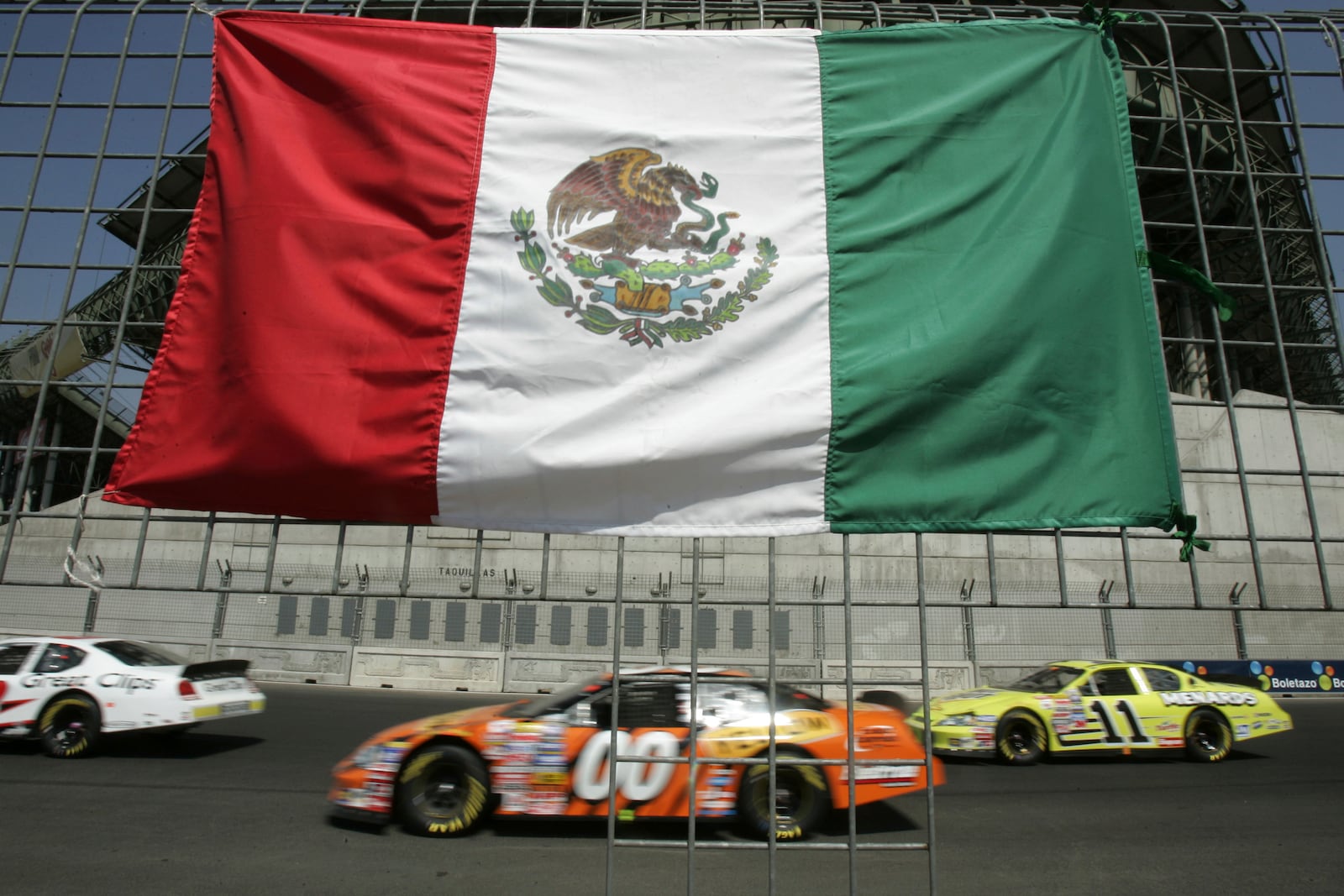 FILE - Cars drive past the flag of Mexico placed at the fence during the NASCAR Busch series auto race at the Hermanos Rodriguez racetrack in Mexico City, Mexico, on Sunday, March 5, 2006.(AP Photo/Gregory Bull, file)