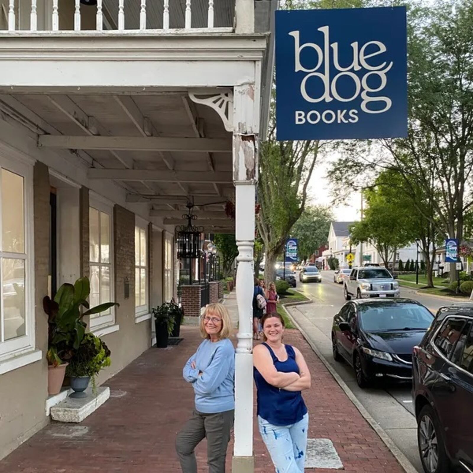 Blue Dog Books owners Deb Covey, left, and Josee Coyle stand underneath the sign outside their bookstore at 245 S. Main St. in historic Springboro. CONTRIBUTED