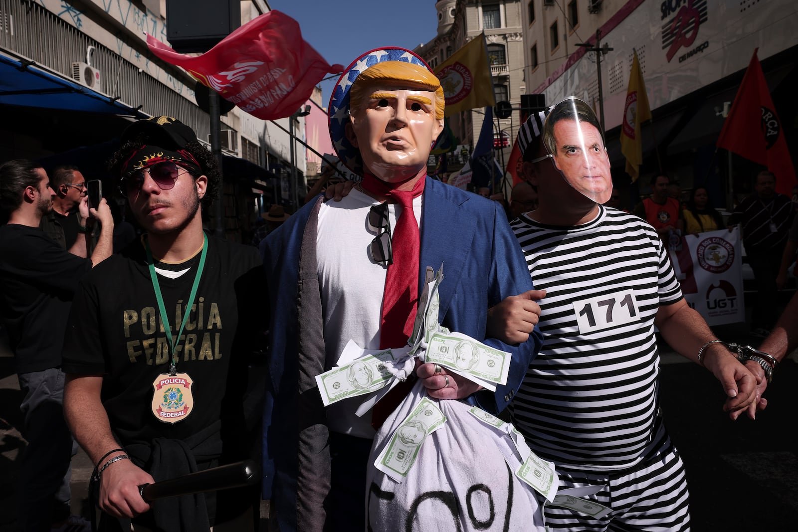 Protesters dressed as police escorting U.S. President Donald Trump and former president of Brazil Jair Bolsonaro demonstrate against Trump's announcement of 50% tariffs on Brazilian goods and against U.S. report that cited counterfeit product sales in Brazil, in Sao Paulo, Friday, July 18, 2025. (AP Photo/Ettore Chiereguini)
