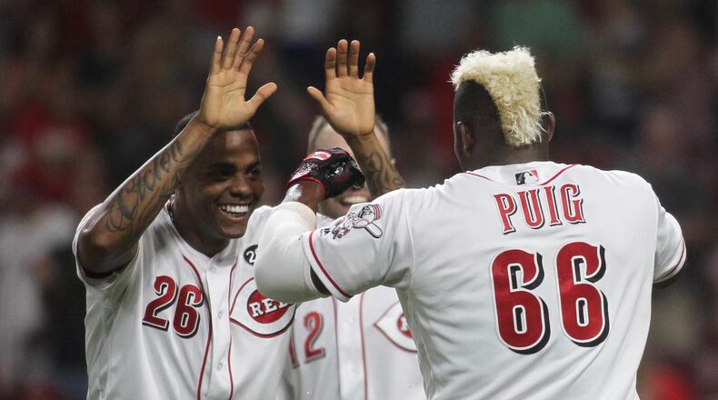 The Reds’ Raisel Iglesias, left, slaps hands with Yasiel Puig after Puig scored the winning run in the 11th inning against the Brewers earlier this month at Great American Ball Park in Cincinnati. David Jablonski/Staff