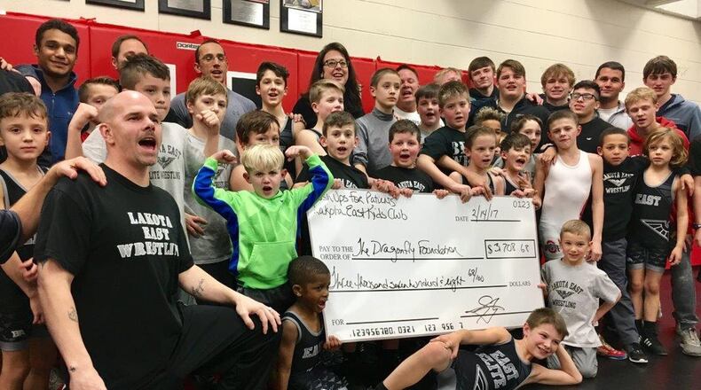 Lakota East High School Youth Wrestling Coach Jay Zurlinden, left, presented a $3,700 check to Dragonfly Foundation co-founder Ria Davidson, back row center, Tuesday evening. Zurlinden’s 10-year-old son Jayden, third from right first row standing, is a cancer survivor and now wrestler. MICHAEL D. CLARK