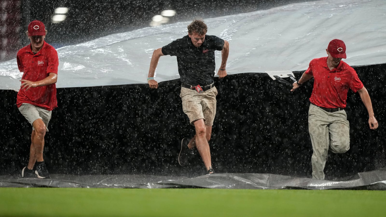 A rain delay is called as members of the grounds crew rush to cover the field as heavy rain falls in the sixth inning of a baseball game between the Cincinnati Reds and the Minnesota Twins, Wednesday, June 18, 2025, in Cincinnati. (AP Photo/Carolyn Kaster)