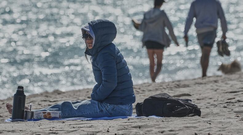 A bundled up Lucia Amato, of Argentina, sits on the shore while waiting for a friend in Miami Beach, Fla., Thursday, Jan. 29, 2026.A bundled up (AP Photo/Marta Lavandier)