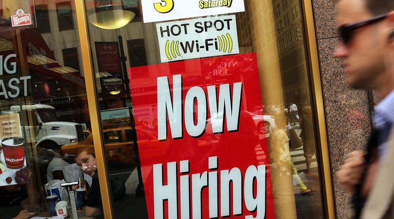 A "now hiring" sign is viewed in the window of a business.