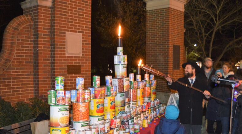 Rabbi Yossi Greenberg lights a candle on the Menorah created with cans of food which were later donated to the Oxford Community Choice Pantry. CONTRIBUTED/BOB RATTERMAN