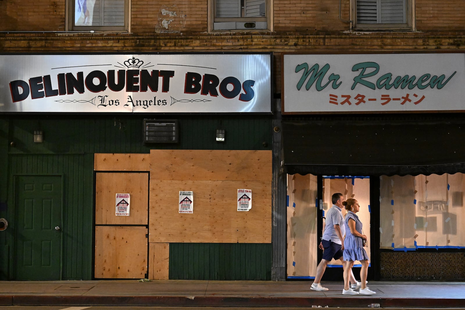 A couple walks past boarded up businesses along 1st St. in Little Tokyo Tuesday, June 17, 2025, in Los Angeles. (AP Photo/Wally Skalij)